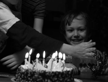 Portrait of smiling boy by birthday cake in darkroom