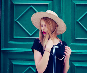 Young woman wearing hat standing against wall