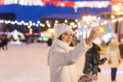 Midsection of woman standing against illuminated building at night during winter