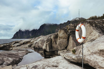 Inflatable ring on pole by rocks against cloudy sky