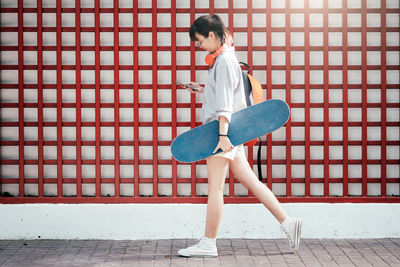 Full length of young woman with skateboard against patterned wall