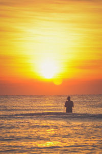 Silhouette man on sea against orange sky