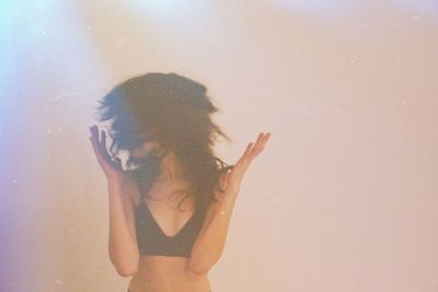 Young woman with arms raised standing against beige wall