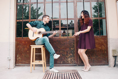 Man playing guitar while friend singing on sidewalk