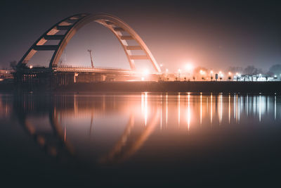 Illuminated bridge over river against sky at night