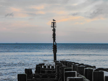 Scenic view of sea and groyne against sky during sunset