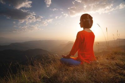 Young caucasian woman meditates in the lotus position in the grass in the mountains near the cliff