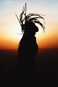 Silhouette woman tossing hair while standing against sky during sunset