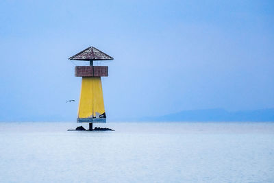 Lighthouse by sea against clear sky