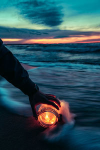 Close-up of hand on illuminated road against sky at sunset