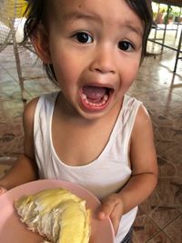 Portrait of cute baby boy screaming while holding food in plate at home