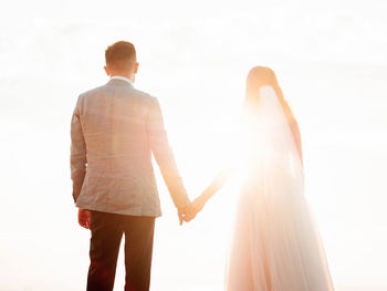 Rear view of newlywed couple standing against sky