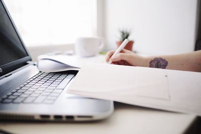 Cropped hands of woman writing at desk in office