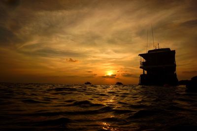 Silhouette ferry boat in sea against cloudy sky during sunset