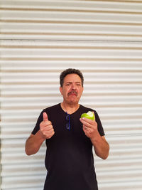 Portrait of man eating apple while standing against wall