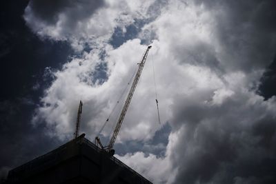 Low angle view of crane by silhouette building against sky