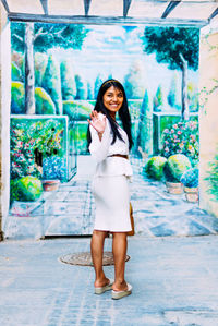 Full length portrait of smiling young woman standing outdoors