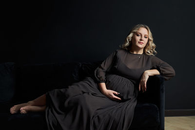 Young woman sitting against black background