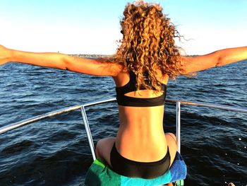 Rear view of woman with arms raised in sea against sky