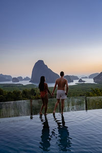 Rear view of people standing by swimming pool against sky