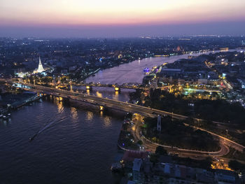 Aerial view of bridge over river in illuminated city at night