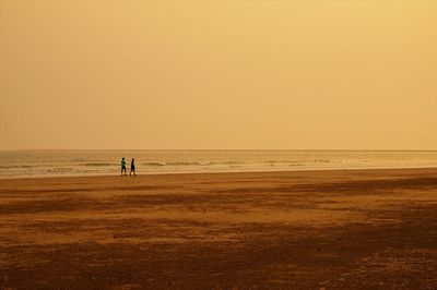 People on beach against clear sky during sunset