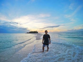 Full length of man walking on beach against sky during sunset