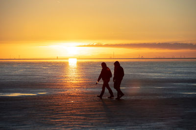 Silhouette men standing on beach against sky during sunset