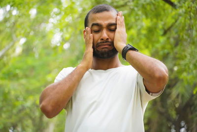 Side view of young man standing against trees