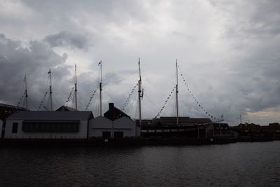 Silhouette buildings by river against sky at dusk