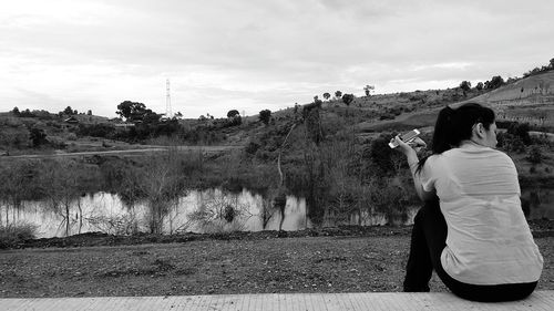 Rear view of woman with phone sitting on boardwalk