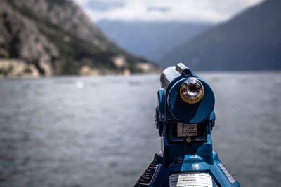 Close-up of coin-operated binoculars by sea against mountain