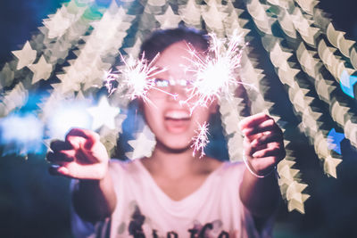 Close-up of young woman burning sparkler at night