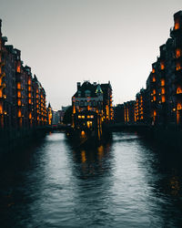 River amidst illuminated buildings against clear sky at dusk