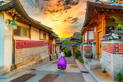 Rear view of woman walking amidst buildings against sky during sunset