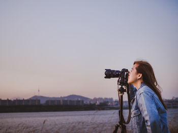 Hipster woman photographer during setting and take photo by her camera to river during sunset