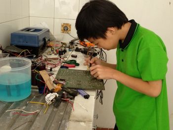 Side view of boy welding circuit at home