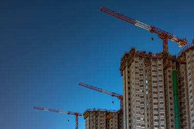 Low angle view of crane by building against clear blue sky