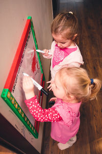 High angle view of cute sisters writing on whiteboard while standing at home