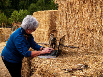 Woman using laptop on hay bales at field