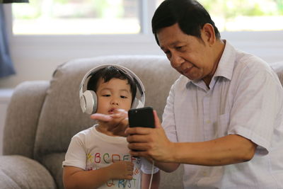 Grandfather and grandson using mobile phone while sitting at home