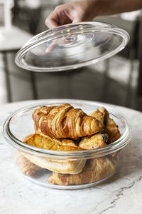 Cropped hand holding lid over container with croissants on table