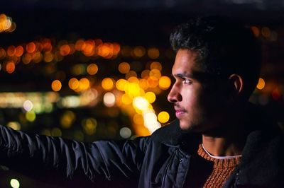 Close-up of young man against illuminated lights