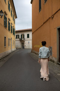 Rear view of woman walking on footpath amidst buildings