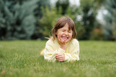 Funny smiling blonde little child girl 4-5 year old lying on green grass lawn outdoor. 