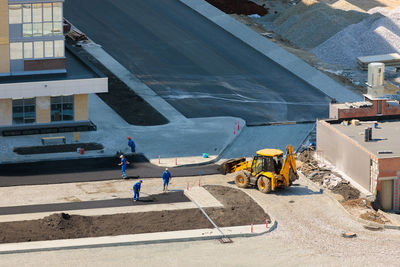 Workers of special equipment are laying asphalt near a house under construction.