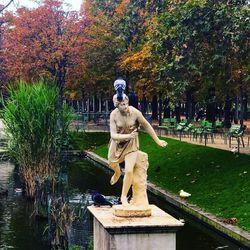 Statue by lake in park during autumn