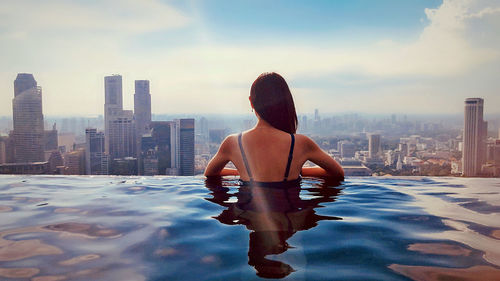 Rear view of man looking at swimming pool against buildings in city