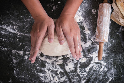 High angle view of cropped hands kneading dough on table
