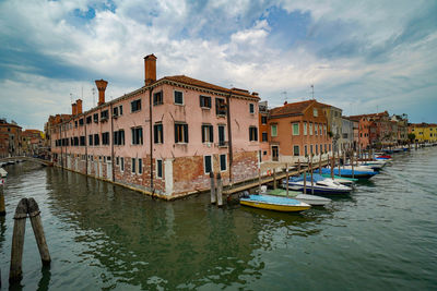 Boats moored in canal by buildings against sky in city